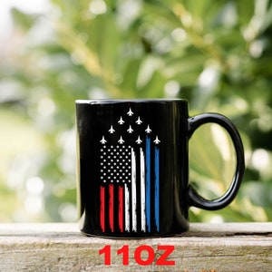 This is a picture of a patriotic coffee mug. The mug is black. The mug has the US flag and a patriotic flyover on one side and on the other side of the mug is a beautiful American Bald Eagle with the American flag