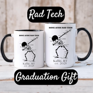 May include: Two white ceramic mugs with black handles and rims. Each mug features a black and white skeleton illustration in a dabbing pose, labeled with bone anatomy terms. The text "Rad Tech" and "Graduation Gift" are also present.