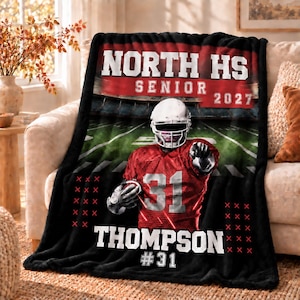 Könnte beinhalten: Eine schwarz-rot-weiße Fleecedecke mit einem Footballspieler im roten Trikot mit der Nummer 31, einem Helm und einem Stadionhintergrund. Der Text lautet NORTH HS SENIOR 2027 und THOMPSON #31 in weißer Schrift auf dem Stoff.