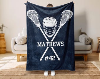 May include: Navy blue fleece blanket with a white lacrosse helmet and two crossed lacrosse sticks. The text "MATHEWS #42" is printed below the sticks.