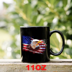 This is a picture of a patriotic coffee mug. The mug is black. The mug has the US flag and a patriotic flyover on one side and on the other side of the mug is a beautiful American Bald Eagle with the American flag