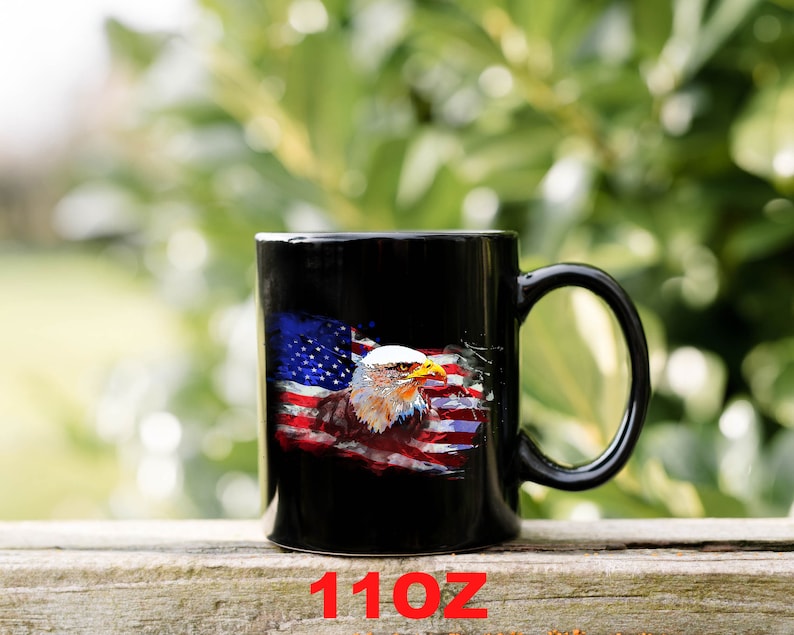 This is a picture of a patriotic coffee mug. The mug is black. The mug has the US flag and a patriotic flyover on one side and on the other side of the mug is a beautiful American Bald Eagle with the American flag