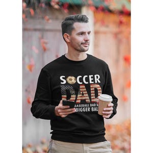 Soccer dad sweatshirt with American flag design and soccer ball graphic, funny soccer dad pullover worn outdoors in autumn setting