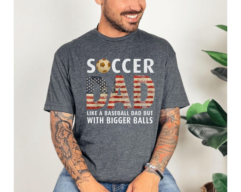 Funny soccer dad t shirt with American flag design and soccer ball graphic, men’s gray tee worn by model in studio setting
