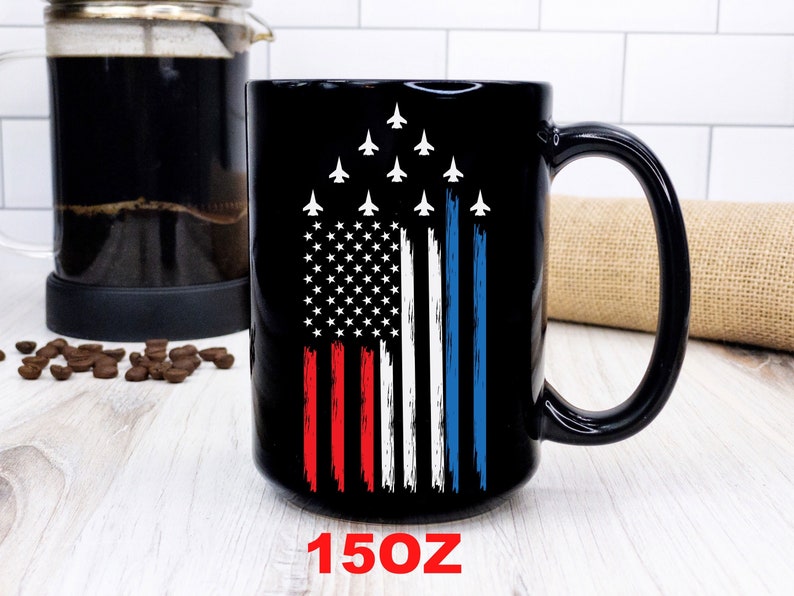 This is a picture of a patriotic coffee mug. The mug is black. The mug has the US flag and a patriotic flyover on one side and on the other side of the mug is a beautiful American Bald Eagle with the American flag
