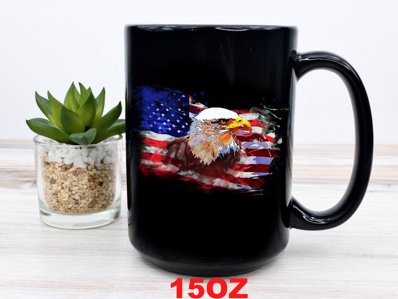 This is a picture of a patriotic coffee mug. The mug is black. The mug has the US flag and a patriotic flyover on one side and on the other side of the mug is a beautiful American Bald Eagle with the American flag