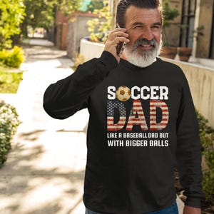 Men’s soccer dad sweatshirt with American flag design and soccer ball graphic, funny soccer dad gift worn in casual outdoor setting