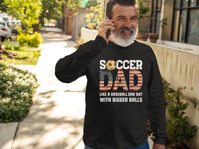 Men’s soccer dad sweatshirt with American flag design and soccer ball graphic, funny soccer dad gift worn in casual outdoor setting