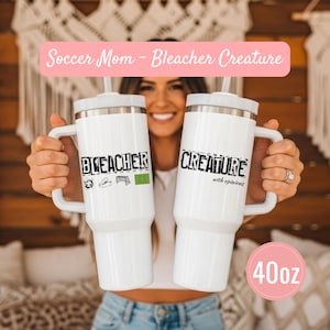 May include: Two white 40oz insulated tumblers with handles. One tumbler reads "Bleacher" with soccer-themed graphics, the other reads "Creature with opinions". A pink banner above reads "Soccer Mom - Bleacher Creature".