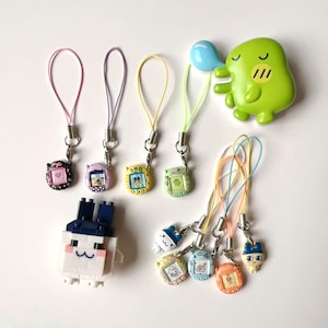 May include: A collection of small digital pet keychains in various colours including black, purple, yellow, green, white, blue, and orange, featuring screen displays and attached lanyards. A green character figure and a white block-built figure are included.