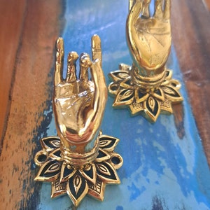 Op de afbeelding: Twee gouden handvormige wandhaken met een zwart lotusontwerp. De haken zijn gemaakt van metaal en hebben een glanzende afwerking.