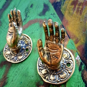 Könnte beinhalten: Zwei goldfarbene Wandhaken in Form von Händen mit verzierten floralen Details um die Basis.