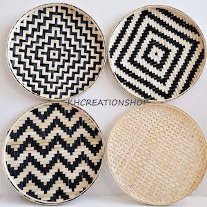 May include: Set of four round woven bamboo wall decor plates. Two plates feature a black and white geometric pattern, one plate has a black and white chevron pattern, and one plate is natural bamboo.