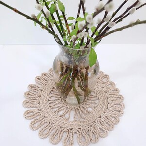 May include: A glass vase with pussy willow branches in it, sitting on a round, beige, woven coaster.