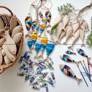 K&ouml;nnte beinhalten: Eine Sammlung von Fischornamenten aus Holz, teils naturbelassen, teils handbemalt mit bunten Mustern in Blau, Gelb, Rot und Orange. Das Set enth&auml;lt einen Weidenkorb, zahlreiche Farbtuben und mehrere d&uuml;nne Pinsel f&uuml;r kreative Arbeiten.