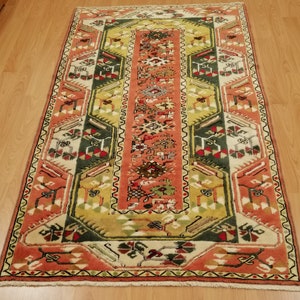 Könnte beinhalten: Ein traditioneller Teppich mit einem geometrischen Muster in Rot-, Grün- und Cremetönen. Der Teppich hat einen Fransenrand und ist aus Wolle gefertigt.