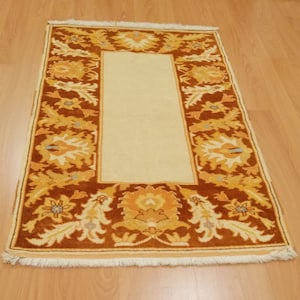 May include: A beige rug with a brown floral border. The rug has a fringe around the edges.