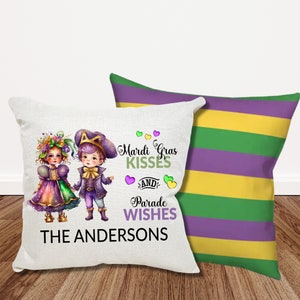 May include: Two children dressed in Mardi Gras costumes stand side-by-side on a white pillow. The boy is wearing a purple and gold costume with a crown. The girl is wearing a purple and gold dress with a flower crown. The pillow has the text "Mardi Gras Kisses and Parade Wishes THE ANDERSONS" printed on it.