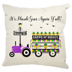 May include: A white throw pillow with the text "It's Mardi Gras Again Y'all!" and a purple tractor pulling a float decorated with green, yellow, and purple beads and tassels. The float has a sign that says "Krewe of Breaux".