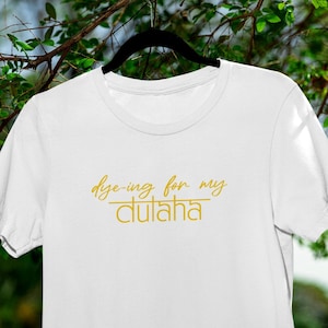 May include: White t-shirt with the text "dye-ing for my dulha" in gold lettering.