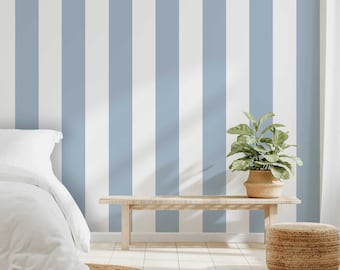 May include: A bedroom with a light blue and white striped wall. A bed with white bedding is on the left. A wooden bench with a plant in a woven basket and a woven ottoman are in front of the wall. A round woven rug is on the floor.