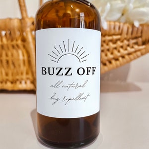 May include: A brown glass bottle with a white label that says "BUZZ OFF all natural bug repellent". The label has a black sun graphic.