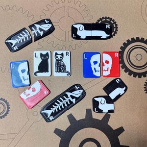 May include: A collection of novelty magnets with various designs. The magnets include a black and white dachshund, a black cat, a skeleton cat, a skull, and a fish skeleton. The magnets are in black, white, red, blue, and white.