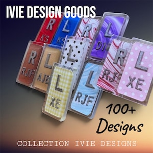 May include: A collection of rectangular acrylic tags featuring various patterns including polka dots, gingham, and marbled designs. Each tag displays a raised metallic letter and smaller initials. Text reads IVIE DESIGN GOODS and 100+ Designs.