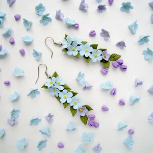 May include: A pair of dangle earrings featuring blue and purple polymer clay flowers. The earrings are made with silver-toned hooks.