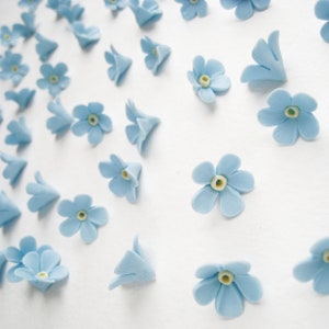 May include: A collection of light blue forget-me-not flower decorations. The flowers are made of fondant and have a yellow centre.