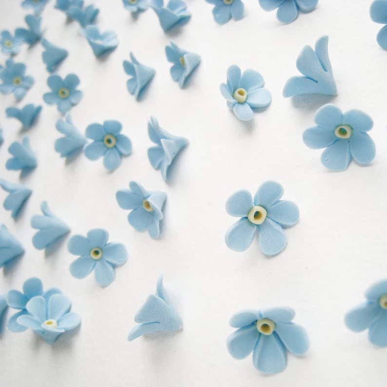 May include: A collection of light blue forget-me-not flower decorations. The flowers are made of fondant and have a yellow centre.