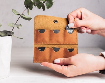 Könnte beinhalten: Ein braunes Lederetui mit sechs Steckplätzen für Speicherkarten. Das Etui ist geöffnet und eine Person hält eine Micro-SD-Karte.