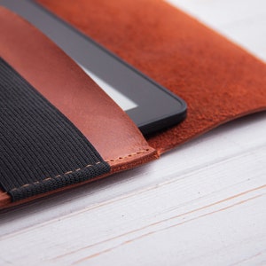 Puede incluir: Una funda de cuero marr&oacute;n para lector electr&oacute;nico con una correa el&aacute;stica negra. La funda est&aacute; cerrada y el lector electr&oacute;nico est&aacute; dentro.