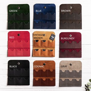 K&ouml;nnte beinhalten: Neun Lederh&uuml;llen f&uuml;r Speicherkarten in verschiedenen Farben, darunter Gr&uuml;n, Blau, Braun, Rot, Vintage Braun, Burgunderrot, Schwarz, Cognac und Grau. Jede H&uuml;lle hat acht Steckpl&auml;tze f&uuml;r Speicherkarten.