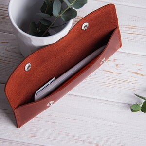 May include: A brown leather pencil case with a silver snap closure. The case is open and a silver pen is inside.