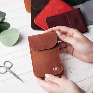 May include: A brown leather pouch with a flap and a single pocket. The pouch has the initials "UC" embossed on the front.