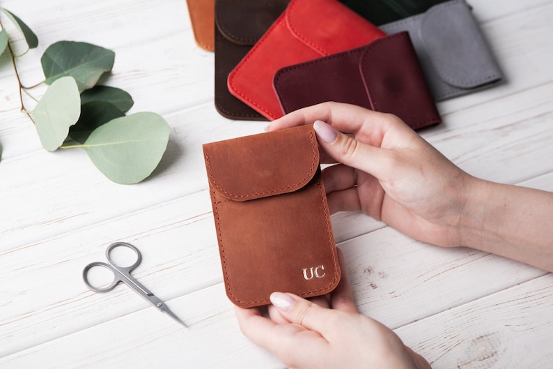 May include: A brown leather pouch with a flap and a single pocket. The pouch has the initials "UC" embossed on the front.
