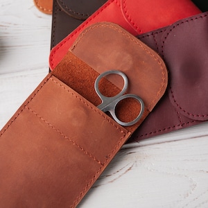May include: A brown leather case with a flap and a small pocket for holding a pair of silver scissors.