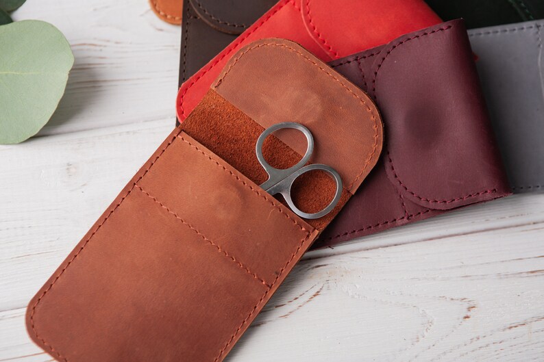 May include: A brown leather case with a flap and a small pocket for holding a pair of silver scissors.