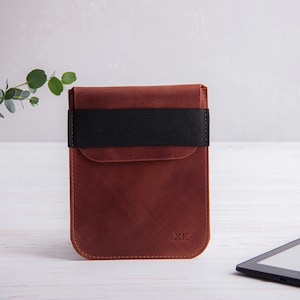 Puede incluir: Una funda de cuero marr&oacute;n con una banda el&aacute;stica negra y las iniciales "XK" grabadas en la parte delantera. La funda est&aacute; dise&ntilde;ada para contener un lector electr&oacute;nico.