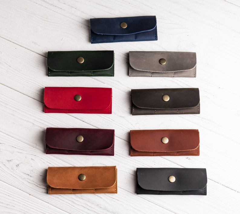 K&ouml;nnte beinhalten: Zehn Leder-Schl&uuml;sselanh&auml;nger in verschiedenen Farben, darunter Rot, Gr&uuml;n, Braun, Blau und Schwarz. Jeder Schl&uuml;sselanh&auml;nger hat einen goldenen Knopfverschluss.