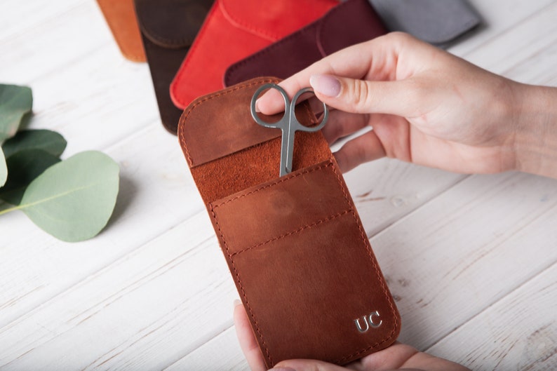 May include: A brown leather case with a small pocket for a pair of scissors. The case has a flap that closes with a snap and has the initials "UC" embossed on the front.