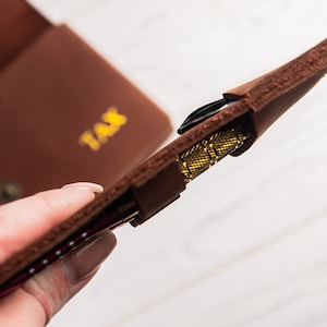 May include: A brown leather case with the word "TAX" embossed on the front. The case is open and a set of darts is visible inside.