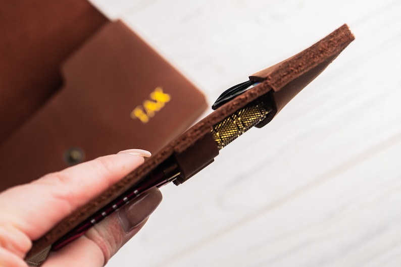 May include: A brown leather case with the word "TAX" embossed on the front. The case is open and a set of darts is visible inside.