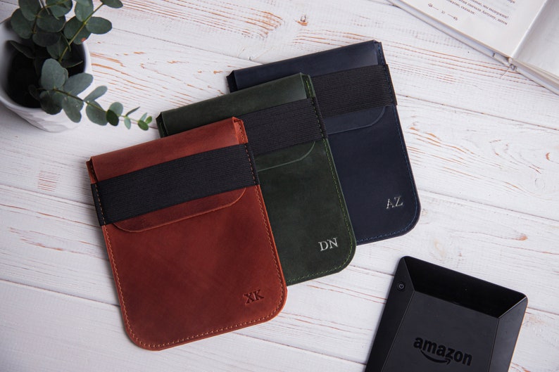 Puede incluir: Tres estuches de cuero en marr&oacute;n, verde y azul con bandas el&aacute;sticas negras e iniciales personalizadas. Los estuches est&aacute;n dise&ntilde;ados para guardar un lector electr&oacute;nico.