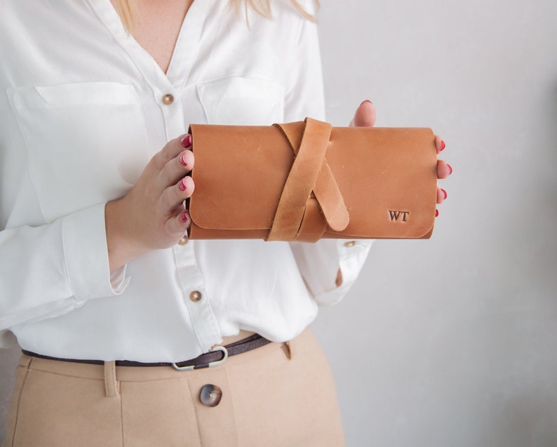 Op de afbeelding: Een bruine leren clutch met een band en de initialen "WT" gegraveerd op de voorkant.
