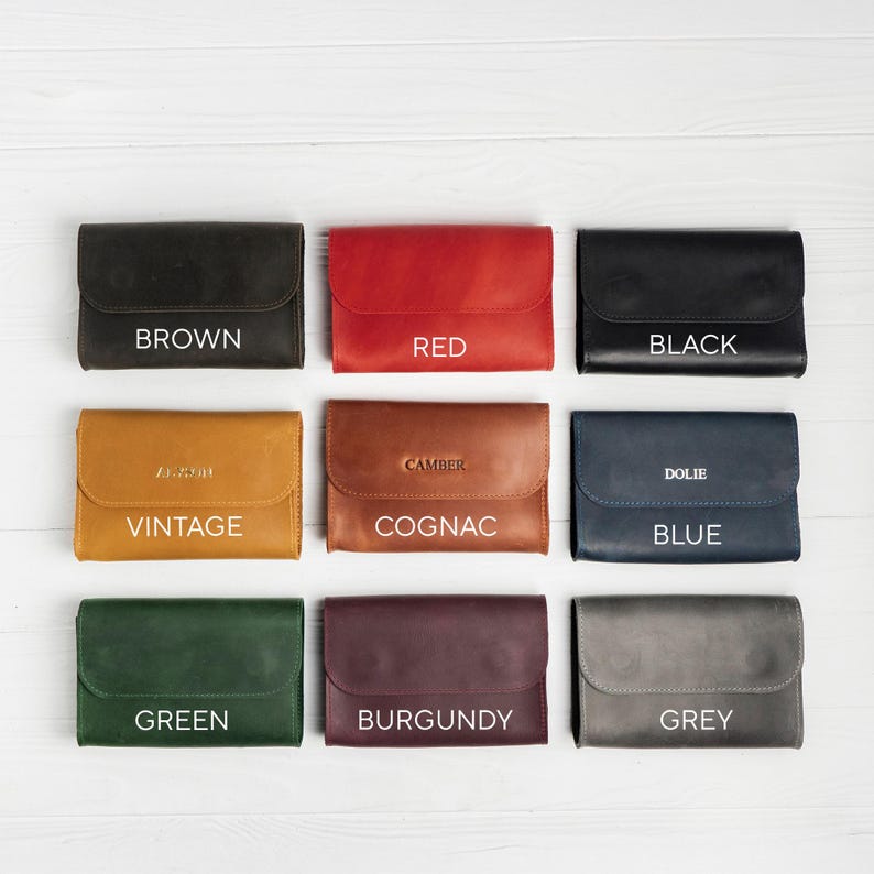 May include: Nine leather wallets in various colors, including brown, red, black, vintage, cognac, blue, green, burgundy, and grey. Each wallet has a flap closure and is labeled with its color name in white text.