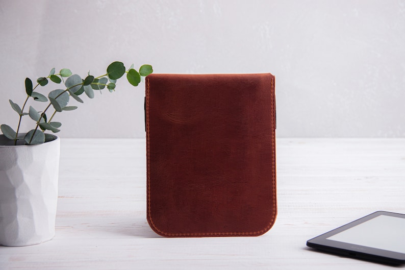 Puede incluir: Una funda de cuero marr&oacute;n para un lector electr&oacute;nico, sobre un fondo blanco.