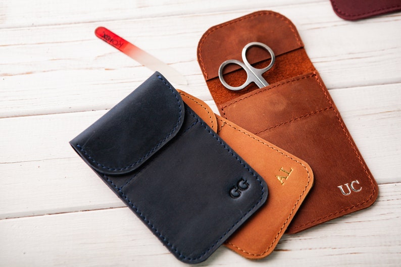 May include: Three personalized leather pouches with different initials, one with a pair of small scissors inside. The pouches are brown, blue, and tan.