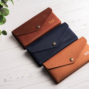 May include: Three leather wallets in brown, blue, and brown with gold lettering. The wallets are personalized with the initials "TAX", "MAX", and "MX".